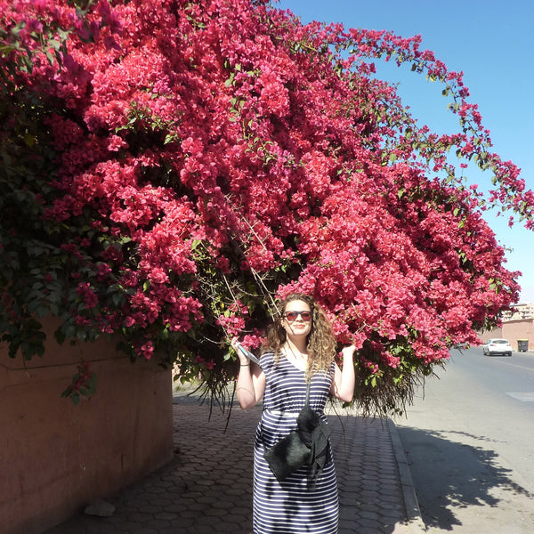 Dark pink Borgainvillea against a blue sky, with woman standing beneath it 