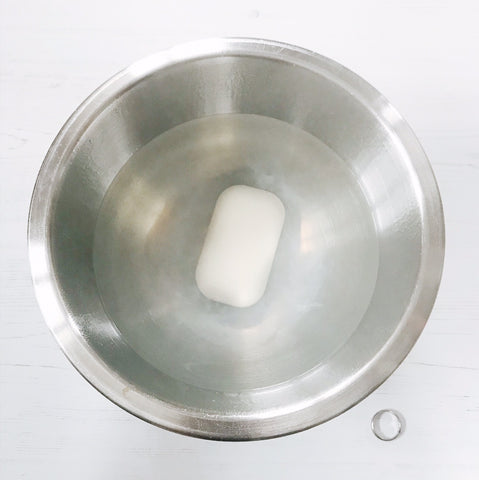 A bar of soap in a bowl of boiling hot water a silver ring by its side