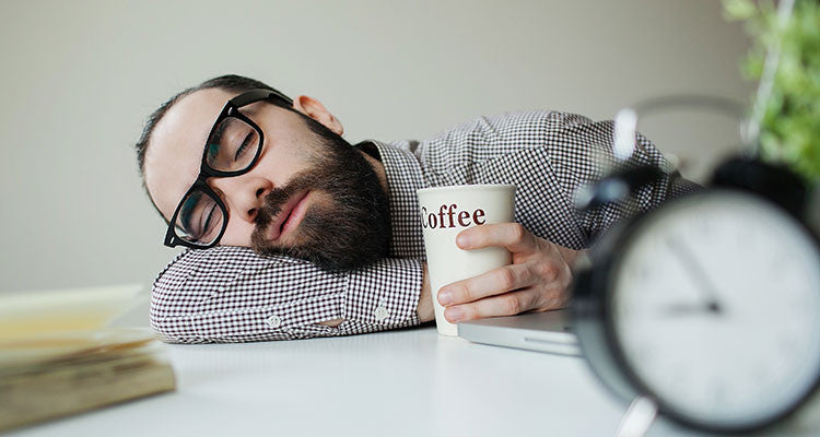 Man Taking A Caffeine Nap At His Desk With Coffee In Hand