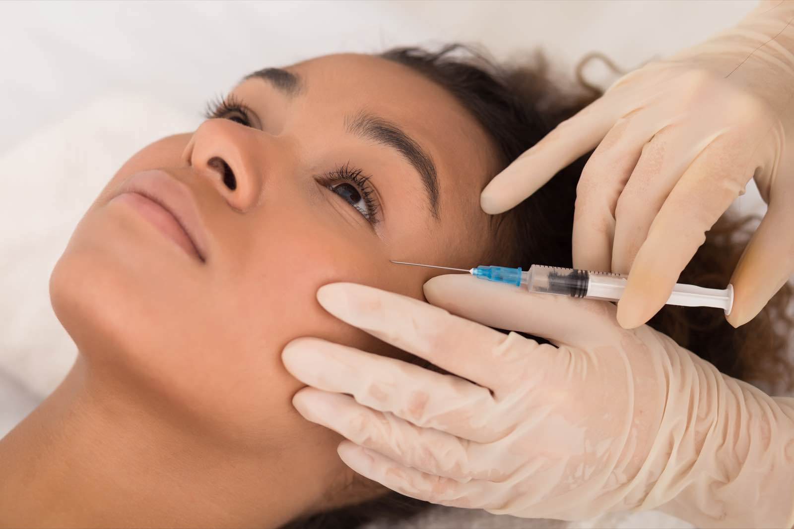 Woman laying on her back receiving an under eye filler injection from a licensed aesthetician