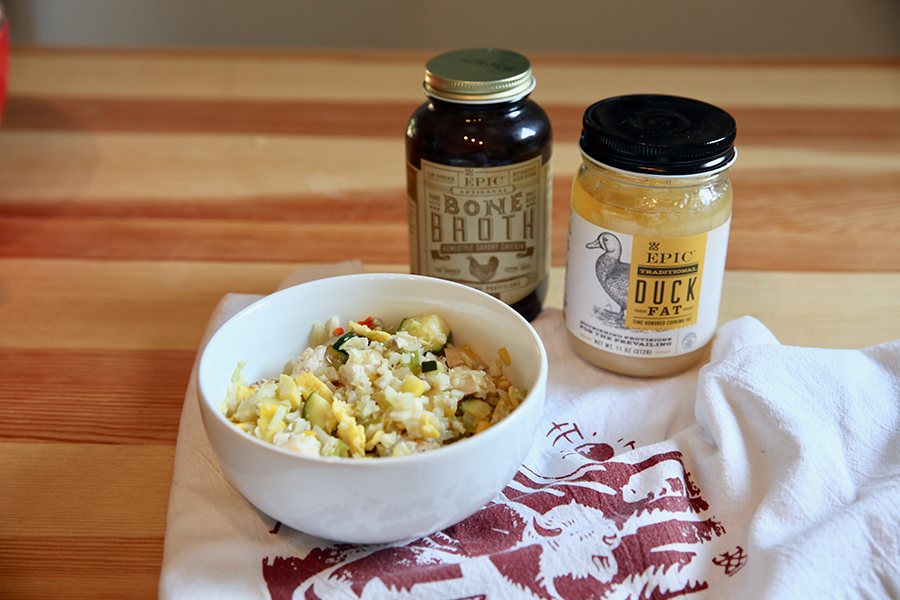 A bowl of cauliflower rice stir fry set next to a jar of EPIC duck fat and EPIC Homestyle Chicken broth.