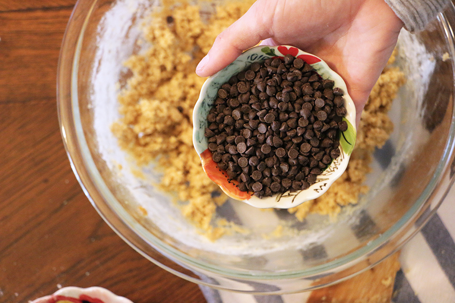 Hand pouring chocolate chips in a bowl of crushed up EPIC Pork Cracklings.