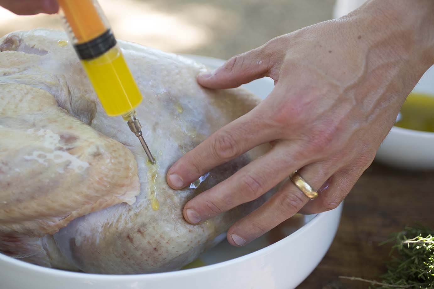 Hands are shown injecting a gold marinate into the turkey