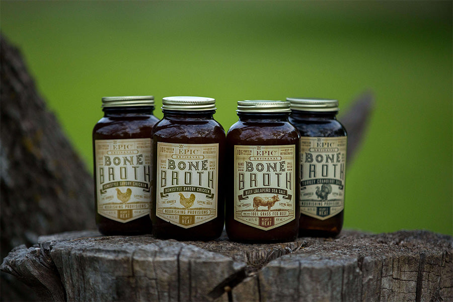 Four jars of bone broth in different flavors sitting on a log