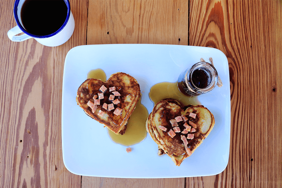 Two stacks of heart-shaped pancakes topped with syrup and EPIC bacon bits