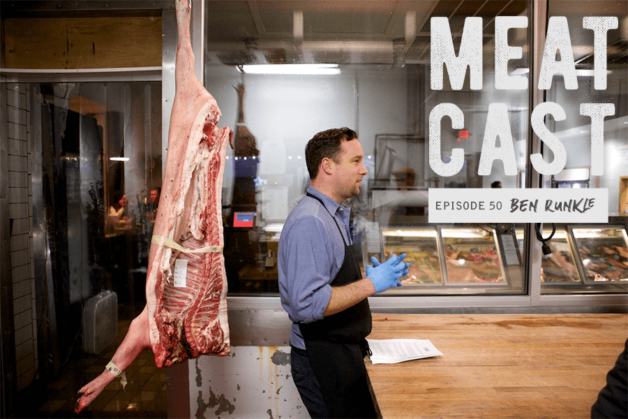 Butcher standing next to hanging carcass in kitchen 