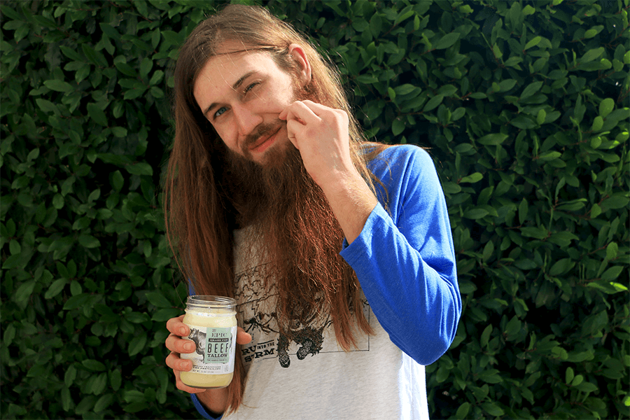 Man with long hair and facial hair putting animal oil on his mustache 