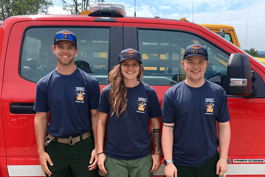 Three firefighters standing in front of a red truck  