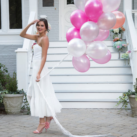 Bride wearing tea length flowy breezy white romantic strapless wedding dress to outdoor shower with balloons