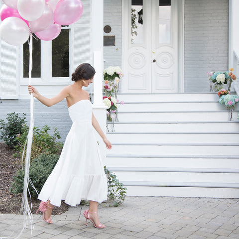 Bride walking with balloons in flowy rustic romantic ruffled tea length white strapless rehearsal dinner dress 