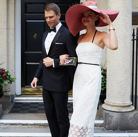 Bride wearing Jane Summers strapless white lace tea length civil ceremony wedding dress and pink hat with black feathers with groom in black tuxedo