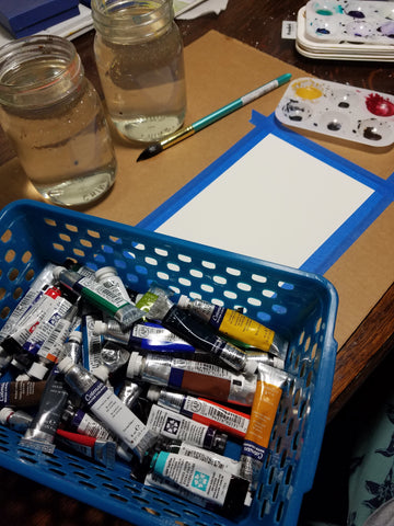Watercolor painting set-up with basket of watercolor tubes