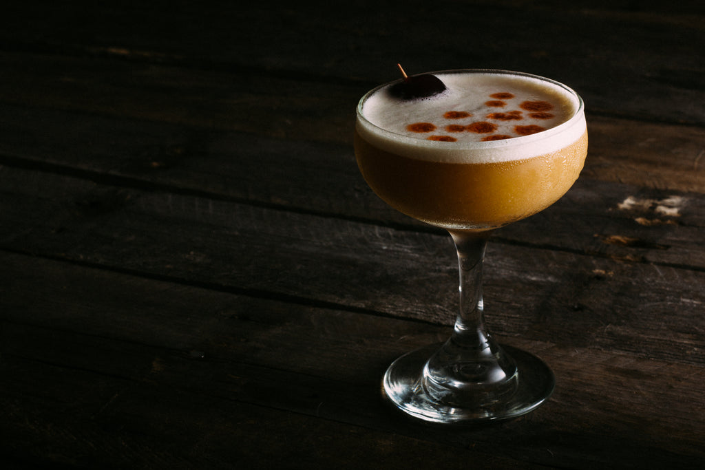 Delicious whiskey sour with conifer simple syrup, egg white, bitters and maraschino cherry