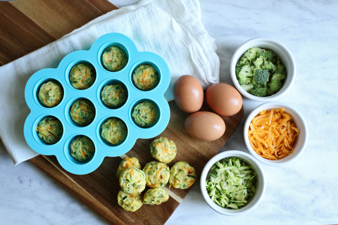baby food freezer tray with fritters beside it and ramekins filled with cheese, broccoli, and eggs