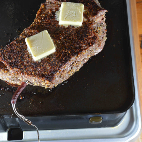 A buttered steak searing to perfection on the Cinder Grill