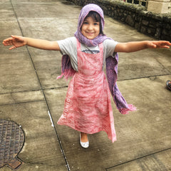 Little girl dressed in an adorable organic cotton natural dyed pink pinafore maxi dress smiling and twirling 