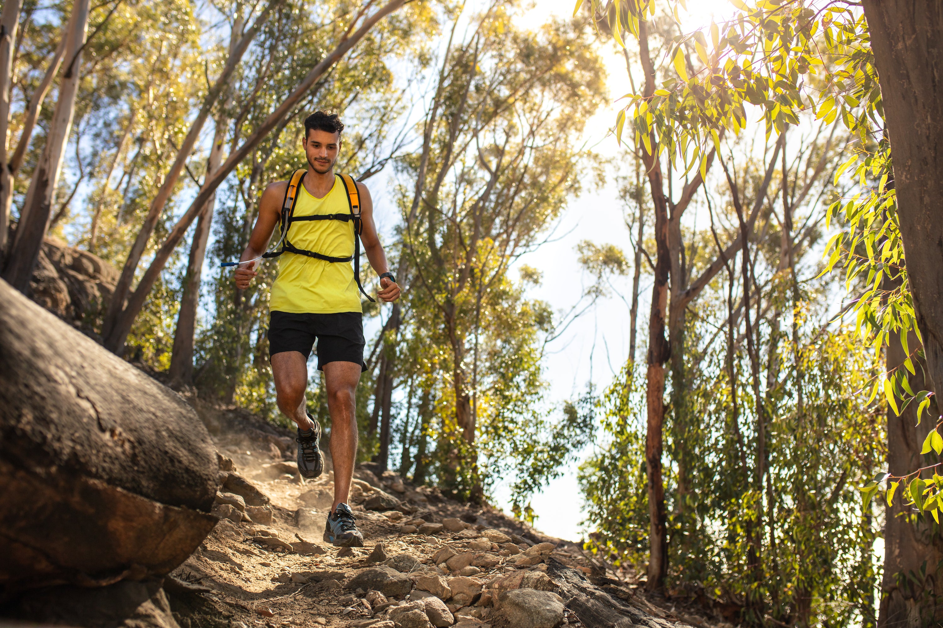 young fit man running down wooded trail with camelbak