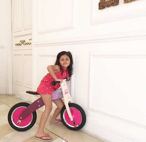 Toddler girl on a Janod wooden cycle. Sustainable toys
