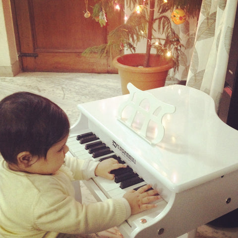 Little cute baby girl playing a white acoustic piano