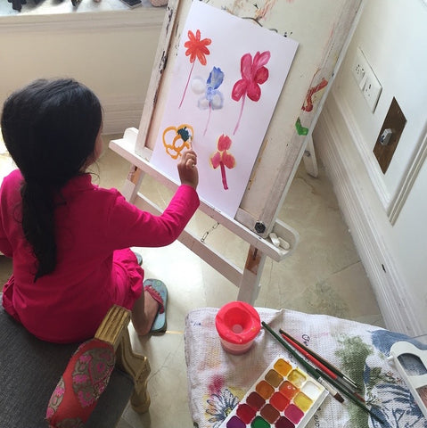 little girl painting with watercolors at home on an art easel.