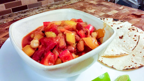 bowl of vegetable chili in bowl on plate with tortillas and limes