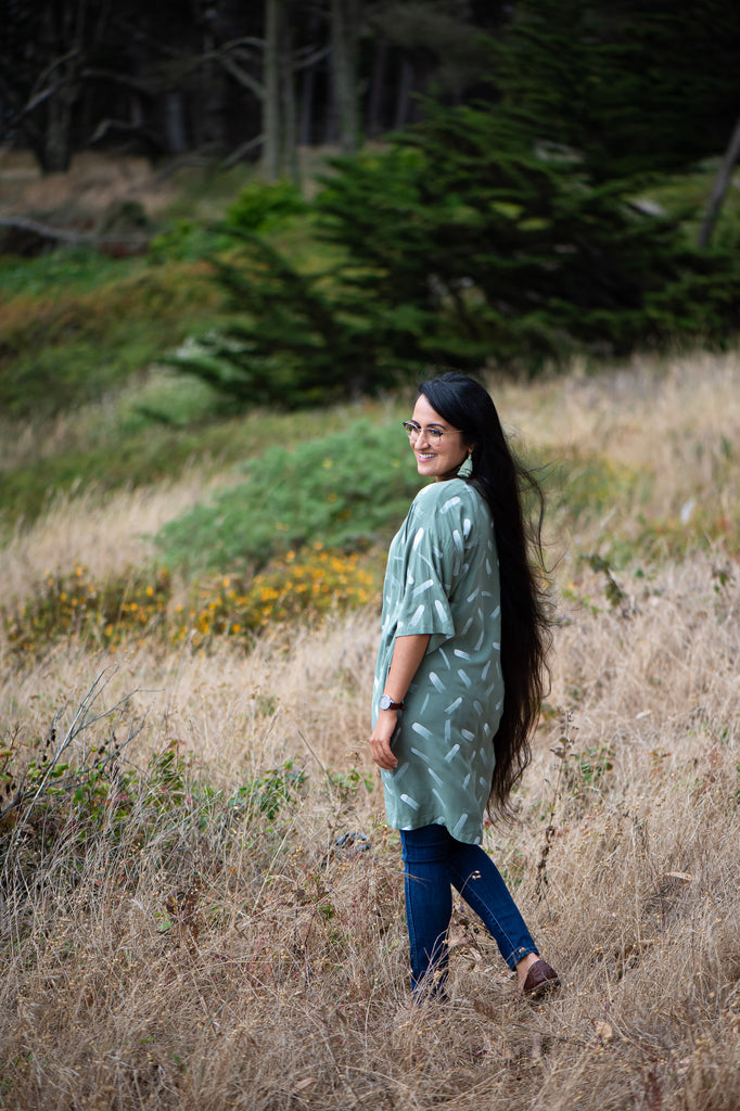 Manpreet Kalra wearing a sage green dress with white dashes by tonlé, she is standing in a field and looking back