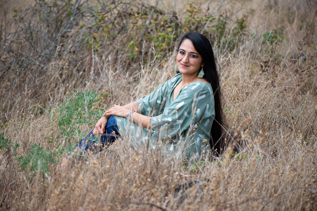 Manpreet Kalra wearing a sage green dress with hand-painted design sitting in a field