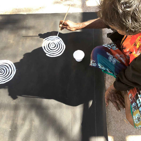 Aboriginal artist Betty Mbitjana leans over canvas to paint concentric circles