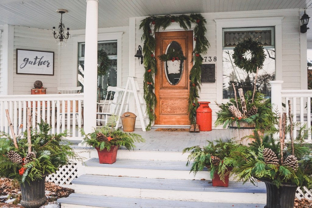 Gorgeous front porch with winter green decorations and a welcoming Gather Personalized Print hanging on the wall.