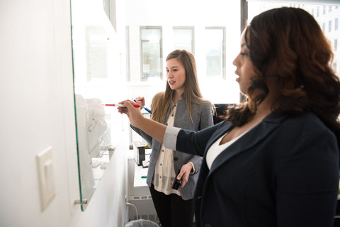 two women being productive by writing on white board 