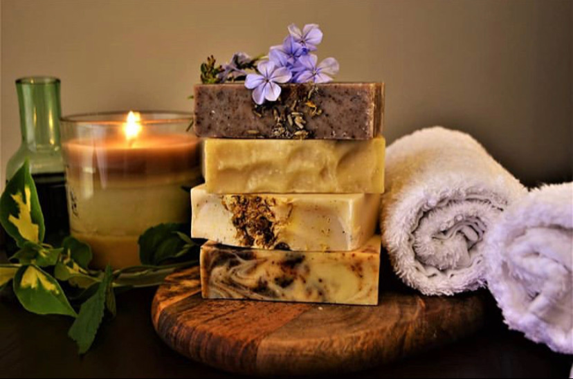 Spa themed picture of 4 luxuriously hand crafted soaps made by YellowBerry with a backdrop of towels and a candle