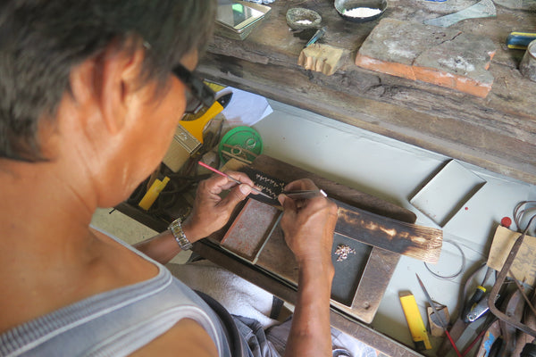 An artisan, also known as a platero, preparing gold filigree parts with tweezers and a pointed tool.