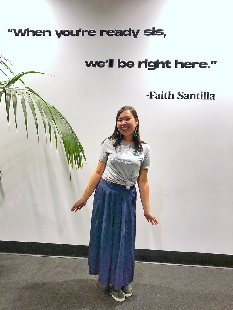 Gelaine Santiago, Social Entrepreneur and Co-Founder of Cambio & Co., standing beneath a sign that says 'when you're ready sis, we'll be right here' by Faith Santilla, at the Pinayista Summit 2019 in San Francisco