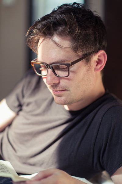 Man Reading A Book With Blue Light Blocking Computer Gaming Glasses Before Going To Sleep