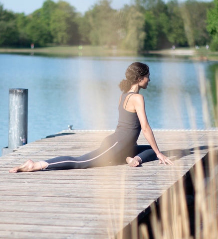 Yogalehrerin Anja Weiß macht eine Taube (Yoga Asana) auf einem Steg und trägt ein Outfit von Mandala Fashion