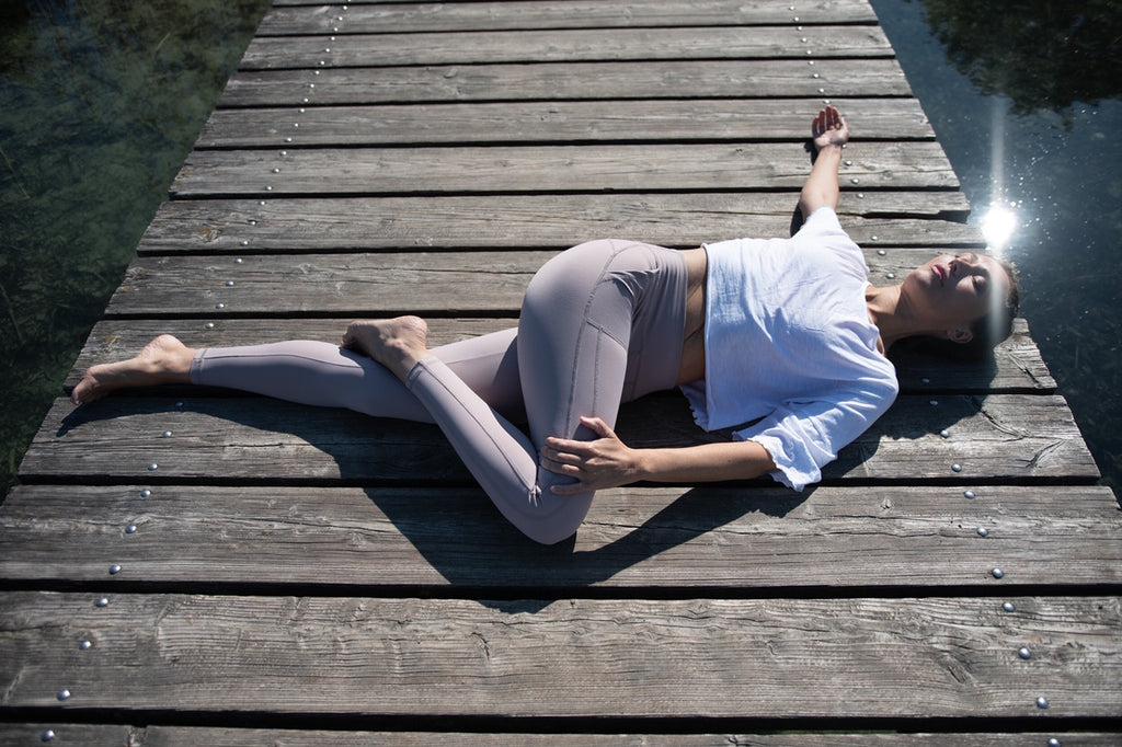 Yogalehrerin Anja Weiß macht eine liegende Drehhaltung (Yoga Pose) auf einem Steg und trägt ein Outfit von Mandala Fashion