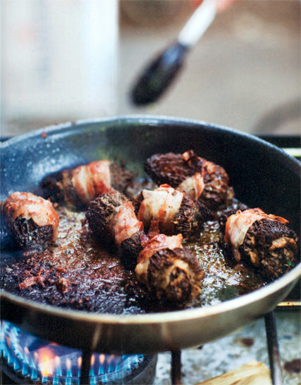 Saute pan of Bacon-Wrapped Duck-Stuffed Morels over a flame