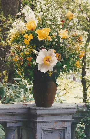 A tall rustic vase of herbaceous peonies, roses, alstroemeria, aster, larkspur.