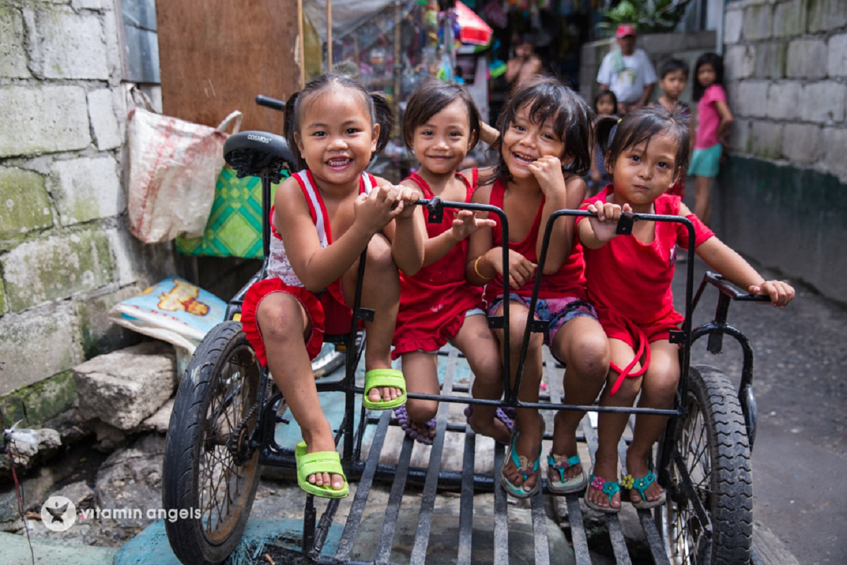 Four little girls wearing a red sleeveless shirt while smiling and riding in the sidecar of a bike