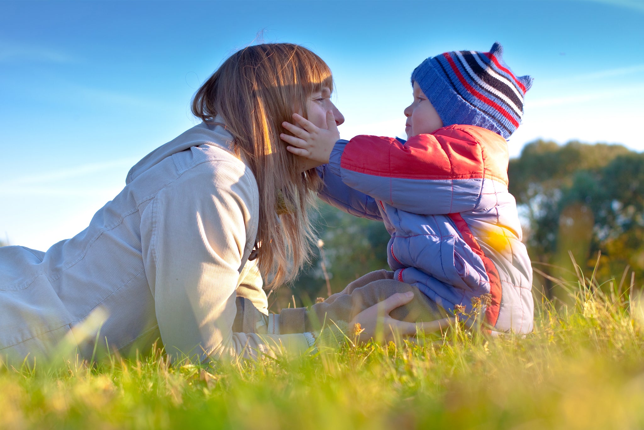 Mother and child in sunny field, , mom lying in grass holding child, tot sitting holding mom's face