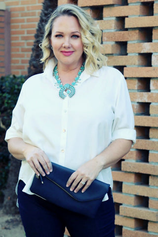 Danielle in a white blouse holding a large navy clutch purse