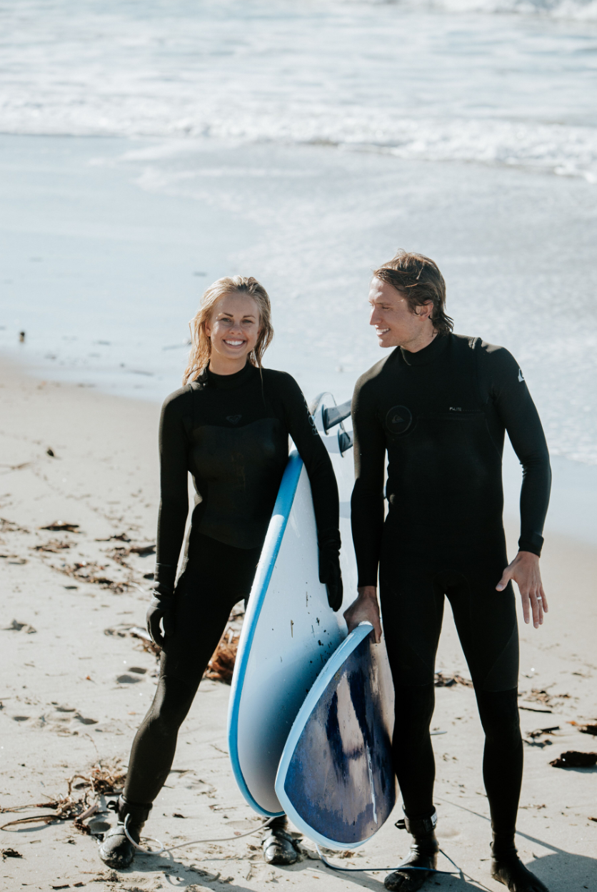 Surfer girl and guy on beach holding their boards