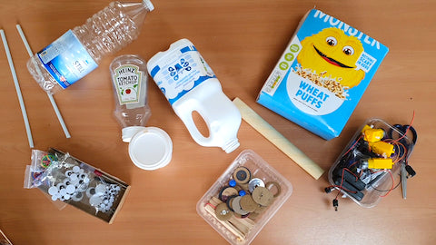 Image of a cereal box, water and milk bottles and some sticks on a wooden table.