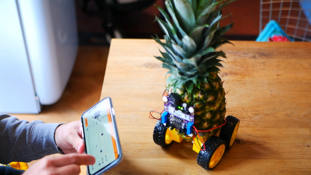Completed pineapple robot with smartphone in foreground showing Smartibot app control pad mapping editor