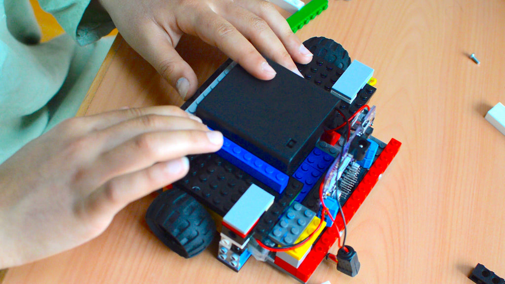 A picture of a two hands assembling a structure around a battery pack with LEGO