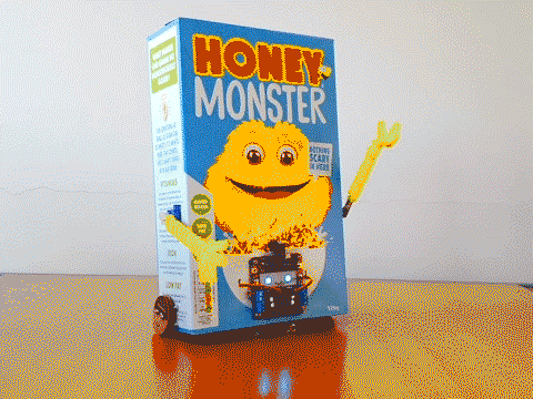 Looping video of a robot made out of a 'Honey Monster' cereal box. The robot waves it's yellow furry arms and then spins around