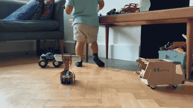 Looping video. First section shows a cardboard robot carrying a smartphone driving towards a small child. Second section shows the robot's point of view with buttons at the side moving it.