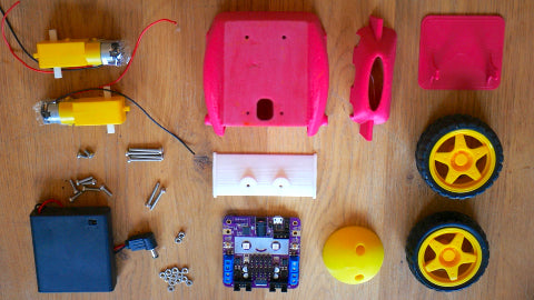 Image of several pink, yellow and white 3D printed (mini) car parts, as well as a pair of yellow and black rubber tires, a purple circuit board, a black battery box, two yellow motors and some screws.
