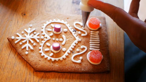 Image of a gingerbread house wall being decorated with white icing and red gumdrops.