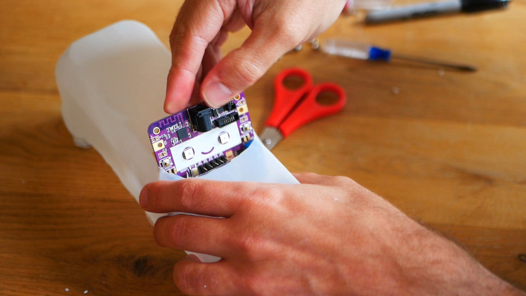 Image of a purple circuit board with a smiley face being put inside a cut milk bottle.